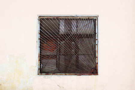 beige wall with a square window behind a thick rusty old grate for background.の写真素材