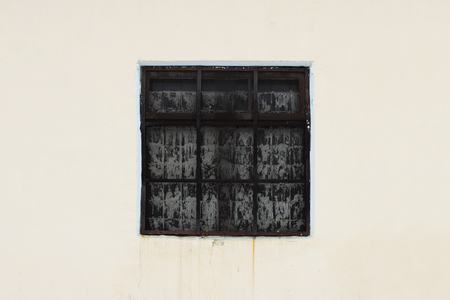 beige wall with a square window behind a thick rusty old grate for background.の写真素材