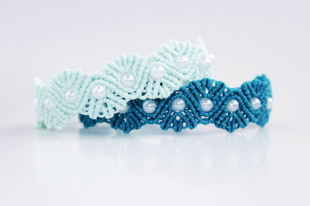 turquoise and blue braceletes with white beads for the hand from waxed thread in the technique of macrame on a white background.の写真素材