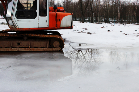 An old rusted excavator stands in a puddle where a tree is reflected. Springの写真素材