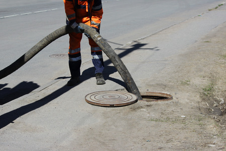 The worker ossenizator pumped sewage out of the sewage system through the hatch in the street. sewerage worker on street cleaning pipeの写真素材