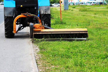 nozzle on a tractor that mows grass on urban lawns. shearing grass near the curb and sidewalkの写真素材