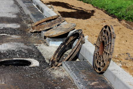 many rusty round hatches and a rainwater grid on the side of the city road. repair and expansion of the road at the exit of the city. Gatchina, Leningrad region, reportage shooting.の写真素材