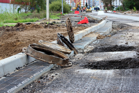 many rusty round hatches and a rainwater grid on the side of the city road. repair and expansion of the road at the exit of the city. Gatchina, Leningrad region, reportage shooting.の写真素材