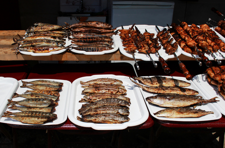 fish whole grilled and meat on skewers cooked entirely on an open fire lie on white trays on the embankment near the Black Sea. Reportage shooting. Republic of Crimea.の写真素材