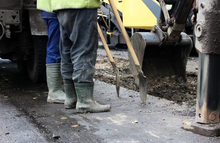 Tractor strong outrigger stabilizing legs extended to stabilize and steady state when digging the soil before applying an asphalt patch on a part of the road during repairの写真素材