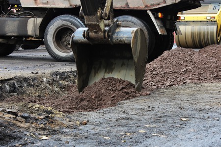Tractor strong outrigger stabilizing legs extended to stabilize and steady state when digging the soil before applying an asphalt patch on a part of the road during repairの写真素材