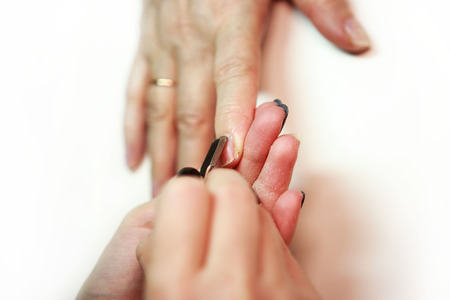 nail service manicurist makes an elderly woman with a metal tool - a lancet with a spatula at the end. Moving off the nail cuticle. reporting shootingの写真素材