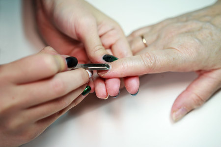 nail service manicurist makes an elderly woman with a metal tool - a lancet with a spatula at the end. Moving off the nail cuticle. reporting shootingの写真素材