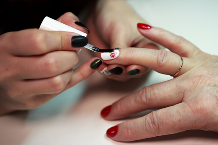 master glues a decal with a rose on the nails on a red and white lacquer manicure. reporting shootingの写真素材