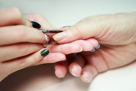 nail service manicurist makes an elderly woman manicure with a metal tool - a lancet with a spatula at the end. Moving off the nail cuticle. reporting shootingの写真素材