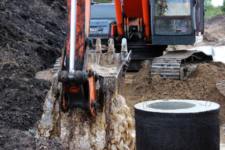 the excavator draws water from the ditch with a bucket where the road will pass. rain season. repair and expansion of the road. storm concrete rings. Gatchina, Russia, reportageの写真素材