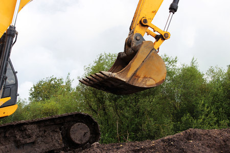 Bucket excavator against a background of green foliage of a tree and blue sky. Road repair extension in Gatchina, Russia. reportageの写真素材