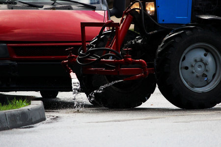 tractor with a barrel on a trailer pours water over the city sidewalks, streams of water flow down to the groundの写真素材