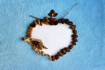 original frame in the form of a heart made of paper, small wooden block, acorns and cones on a blue terry cloth.の写真素材