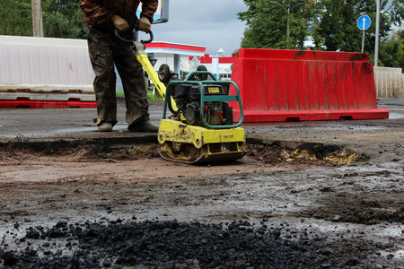 The foreman of the construction team works with a vibrating platform plate, tamping up the sand before the asphalting of the road using the patch method. reportageの写真素材