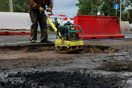 The foreman of the construction team works with a vibrating platform plate, tamping up the sand before the asphalting of the road using the patch method. reportageの写真素材