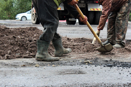 workers with shovels prepare part of the road for asphalting using the patch method. repair and expansion of the road. Gatchina, reportage.の写真素材