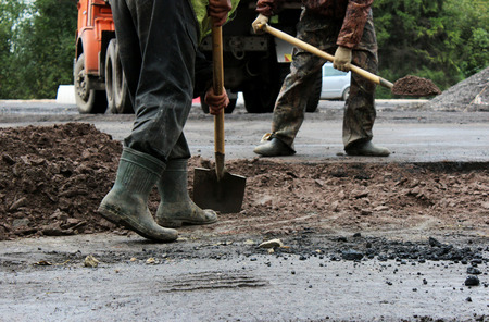 workers with shovels prepare part of the road for asphalting using the patch method. repair and expansion of the road. Gatchina, reportage.の写真素材