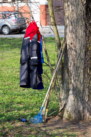 a working jacket, blue fan-shaped rakes and a roll of plastic bags are next to the workers cleaning the territory. spring cleaning.の写真素材