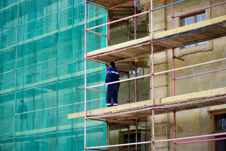 restoration of the Gatchina Palace. worker stands on scaffolding. part of the palace is covered with a protective green grid. reportageの写真素材