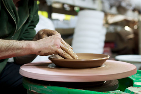 a master ceramist with 13 years of experience makes plate from red clay on a potters wheel, on a sheet of particle board for better removal and further drying. reportage.の写真素材