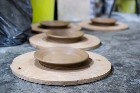 a master ceramist with 13 years of experience maked several plates from red clay on a potters wheel, on a sheet of particle board for better removal and further drying. reportageの写真素材