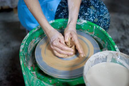 A novice student in the first lesson in pottery tries to make a product from clay on a potter's wheel. reportage. Incorrect hand setting.の写真素材