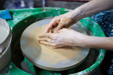 A novice student in the first lesson in pottery tries to make a product from clay on a potter's wheel. reportage. Incorrect hand setting.の写真素材