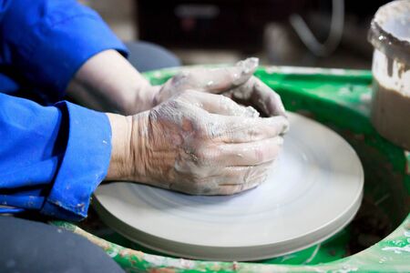 A novice student in the first lesson in pottery tries to make a product from clay on a potter's wheel. reportage. clay centering. Incorrect hand setting.の写真素材