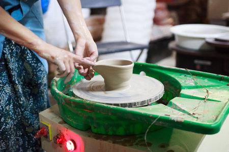 Young woman novice student in the first lesson in pottery tries to make a product from white clay on...