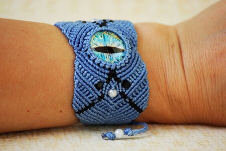 blue bracelete with white beads and the dragon's eye on the hand from waxed thread in the technique of macrame. Handmade. put on hand.の写真素材