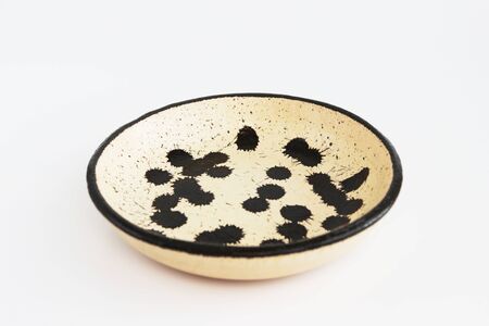 beige clay plate with black spots. made of layer, covered with transparent glaze. two roasting. Handmade ceramics. On a white backgroundの写真素材