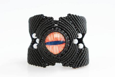 black bracelete with red dragon's eye for arm from waxed thread in the technique of macrame on a white background. Handmade.の写真素材