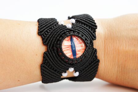 black bracelete with red dragon's eye for arm from waxed thread in the technique of macrame on a white background. Handmade. put on handの写真素材