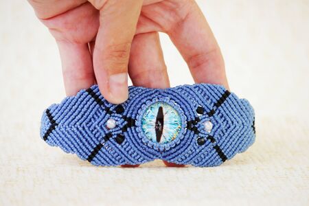 blue bracelete with white beads and the dragon's eye on the hand from waxed thread in the technique of macrame. Handmadeの写真素材