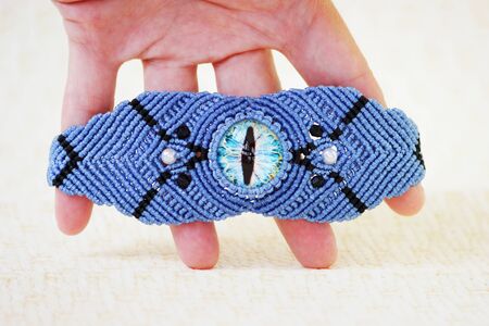blue bracelete with white beads and the dragon's eye on the hand from waxed thread in the technique of macrame. Handmadeの写真素材
