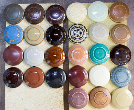 Several round clay samplers with multi-colored glazes on them lie on the square stones after firing.