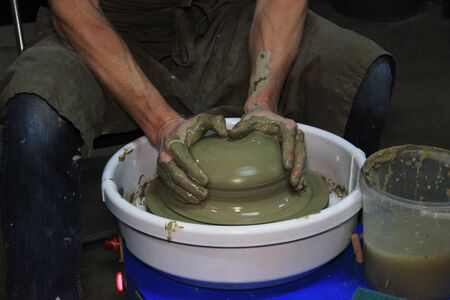 experienced potter makes a large vase on a potter's wheel. twisting a narrow neck. clay product. hands of a potter. reportage shooting. work with a large piece of clayの写真素材