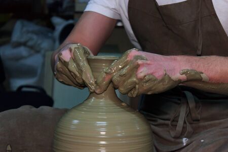 experienced potter makes a large vase on a potter's wheel. twisting a narrow neck. clay productの写真素材
