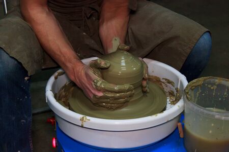 experienced potter makes a large vase on a potter's wheel. twisting a narrow neck. clay product. hands of a potter. reportage shooting. work with a large piece of clayの写真素材