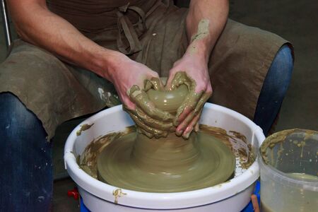 experienced potter makes a large vase on a potter's wheel. twisting a narrow neck. clay product. hands of a potter. reportage shooting. work with a large piece of clayの写真素材