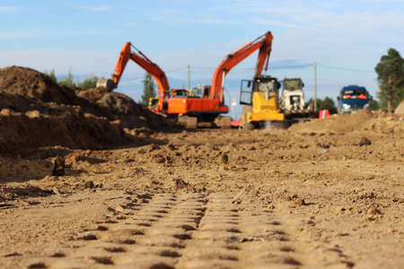 imprints of traces of heavy equipment in the sand. working excavators in the background. repair and construction of a road in the cityの写真素材
