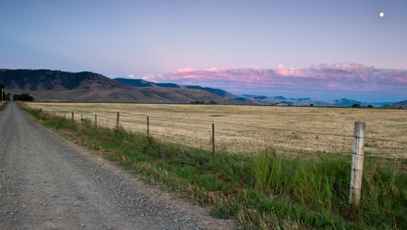 wide open field with the road on one side and the moon and sunset on the otherの写真素材