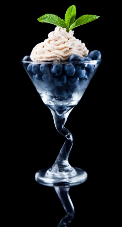 blueberries in a martini glass with fresh cream and green mint as a garnish isolated on a black backgroundの写真素材