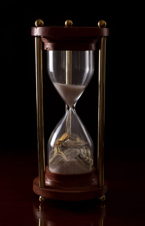 hour glass on a dark background with american money in it