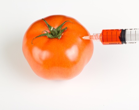 syringe injecting red steroids into a tomato representing gmo products on a white tableの写真素材