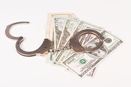 silver handcuffs over federal reserve currency bills on a white background