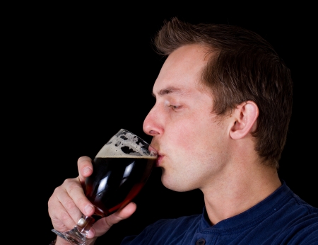 adult male drinking a dark beer isolated on a balck backgroundの写真素材