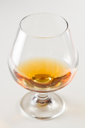 closeup of a brandy snifter on a white table top with a golden reflection to the sideの写真素材